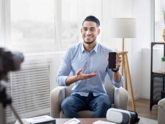 Arab male influencer filming video review of contemporary smartphone on dslr camera at home, mockup on screen
