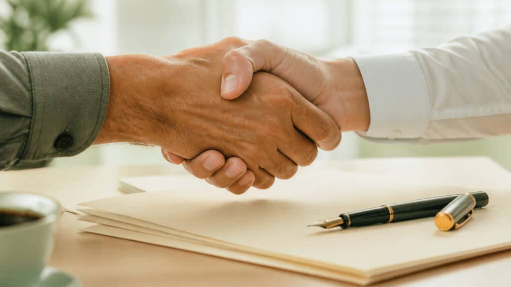 Corporate Handshake Over Stack Of Legal Documents In Bright High Key Daylight With Intimate Overhead Detail